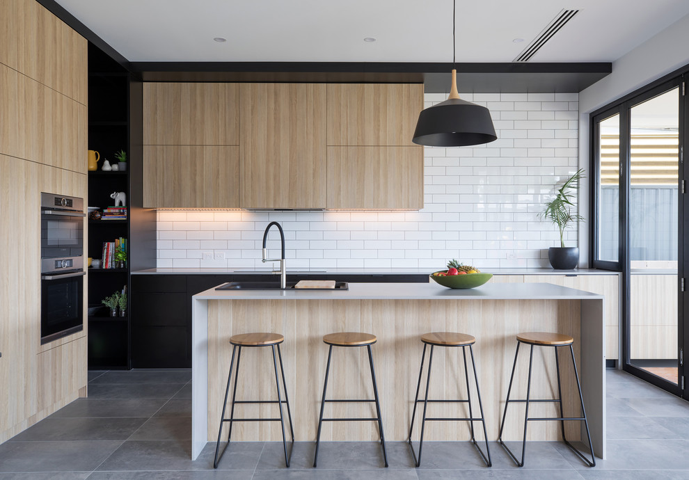 Design ideas for a medium sized contemporary l-shaped kitchen in Adelaide with a double-bowl sink, flat-panel cabinets, light wood cabinets, engineered stone countertops, white splashback, metro tiled splashback, stainless steel appliances, an island and grey floors.