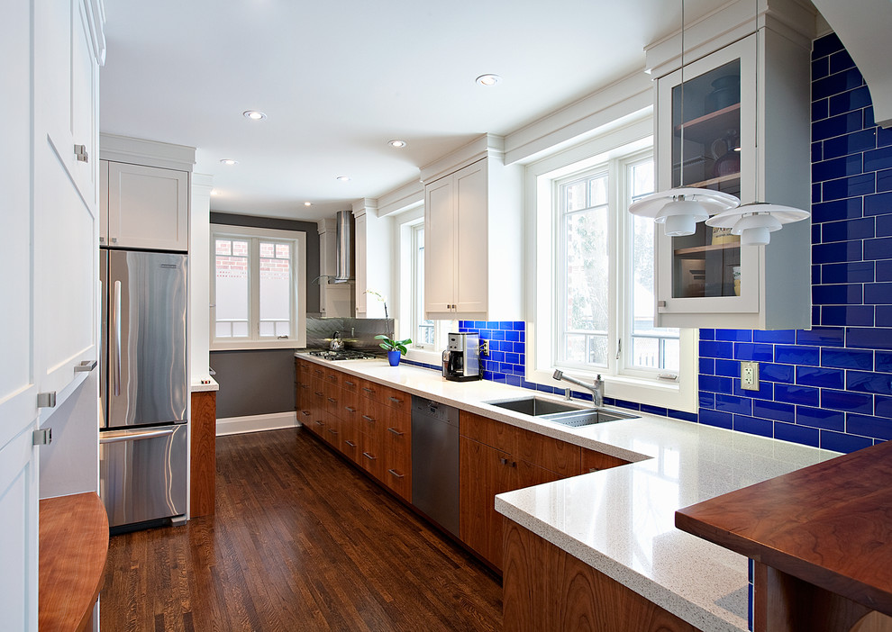 Modern inredning av ett avskilt kök, med blått stänkskydd, stänkskydd i tunnelbanekakel, rostfria vitvaror, en dubbel diskho, skåp i mörkt trä och släta luckor