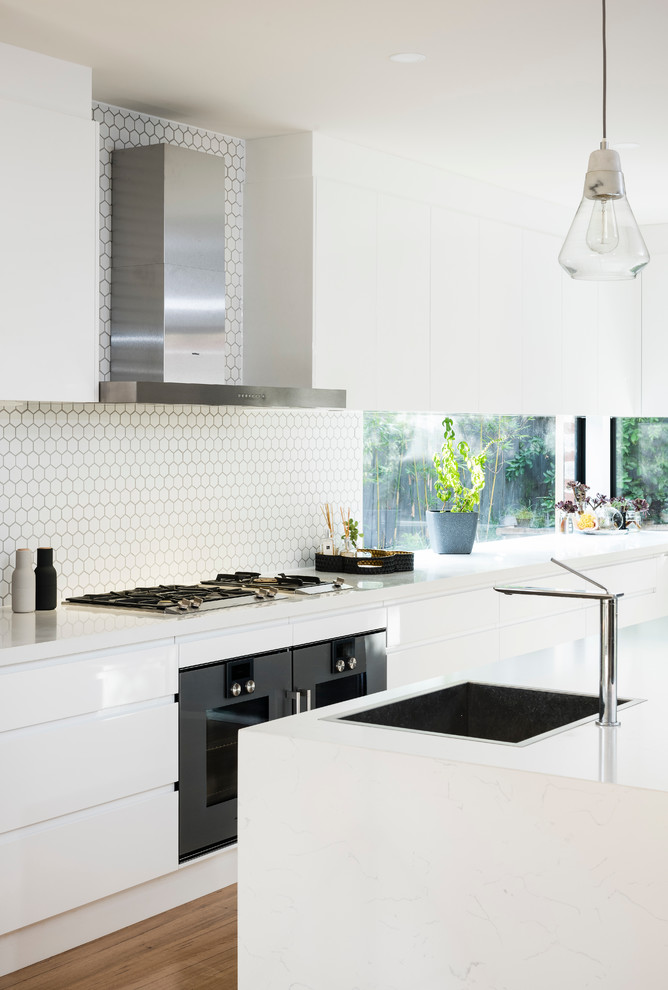 Inspiration for a large contemporary l-shaped medium tone wood floor kitchen pantry remodel in Melbourne with a drop-in sink, flat-panel cabinets, white cabinets, quartz countertops, white backsplash, cement tile backsplash, black appliances and an island