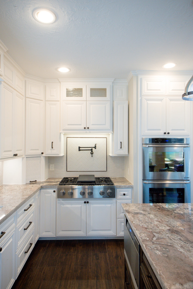 Exempel på ett mellanstort klassiskt kök, med en undermonterad diskho, luckor med upphöjd panel, vita skåp, granitbänkskiva, grått stänkskydd, stänkskydd i keramik, rostfria vitvaror, mellanmörkt trägolv, en köksö och brunt golv