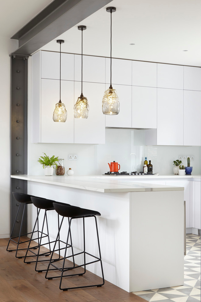 Inspiration for a large contemporary u-shaped open plan kitchen in London with a built-in sink, flat-panel cabinets, white cabinets, marble worktops, white splashback, glass sheet splashback, coloured appliances, concrete flooring and an island.