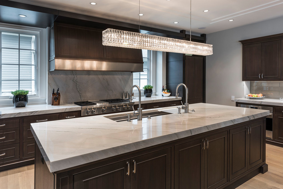 Large trendy u-shaped light wood floor and beige floor enclosed kitchen photo in Miami with an undermount sink, raised-panel cabinets, dark wood cabinets, white backsplash, stone slab backsplash, stainless steel appliances and an island