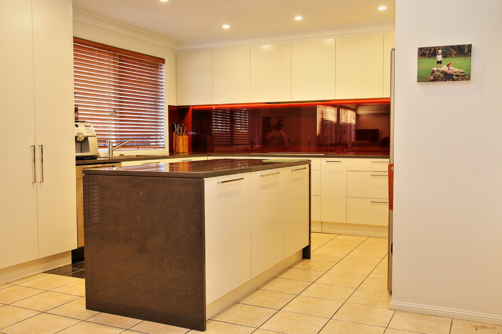 Inspiration for a large modern u-shaped kitchen pantry in Sydney with a built-in sink, flat-panel cabinets, beige cabinets, engineered stone countertops, red splashback, glass sheet splashback, stainless steel appliances, ceramic flooring and an island.