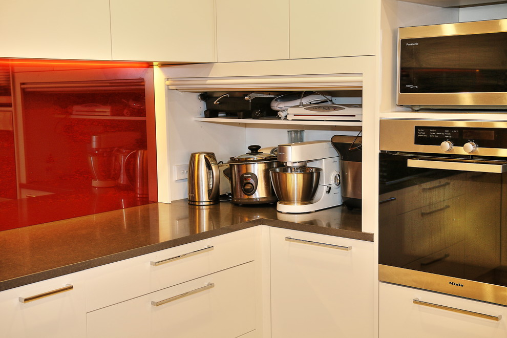 シドニーにあるラグジュアリーな広いモダンスタイルのおしゃれなキッチン (ドロップインシンク、フラットパネル扉のキャビネット、ベージュのキャビネット、クオーツストーンカウンター、赤いキッチンパネル、ガラス板のキッチンパネル、シルバーの調理設備、セラミックタイルの床) の写真