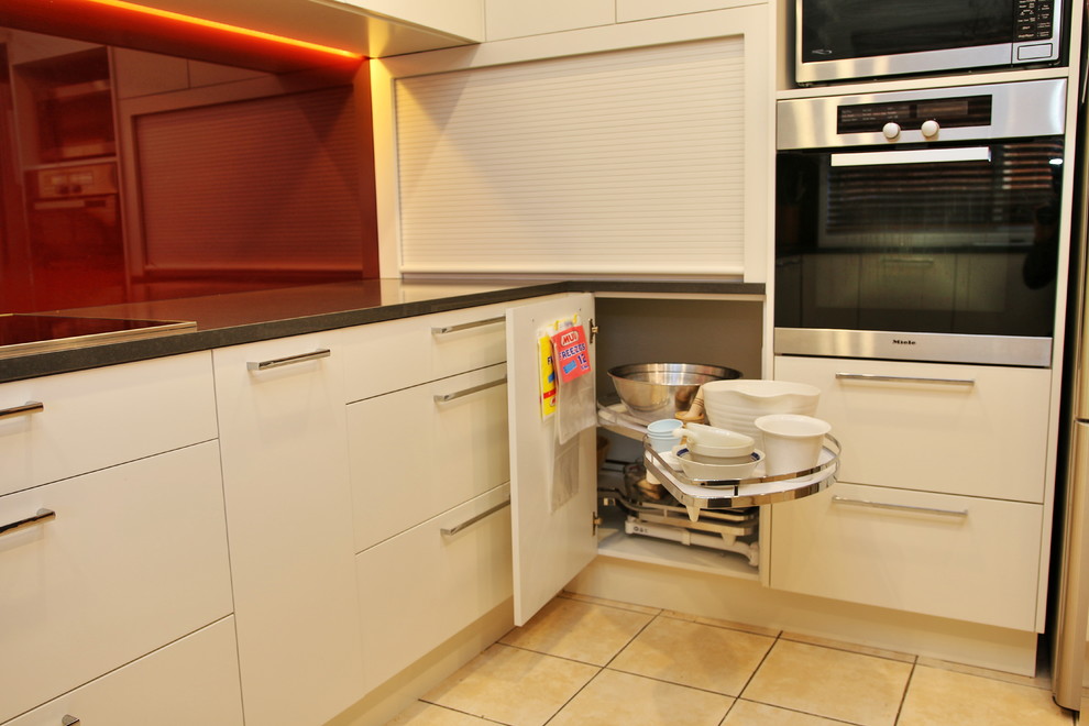 Modern inredning av ett stort kök, med en nedsänkt diskho, släta luckor, beige skåp, bänkskiva i kvarts, rött stänkskydd, glaspanel som stänkskydd, rostfria vitvaror, klinkergolv i keramik och en köksö