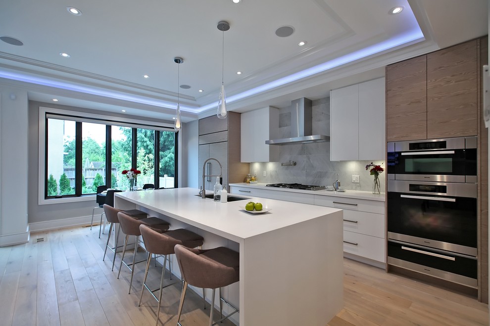 Example of a trendy galley light wood floor eat-in kitchen design in Toronto with flat-panel cabinets, white cabinets, gray backsplash, stainless steel appliances and an island