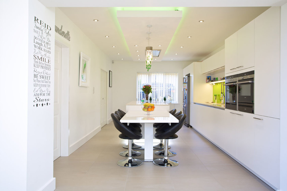Inspiration for a large contemporary galley open plan kitchen in Hampshire with an integrated sink, flat-panel cabinets, white cabinets, composite countertops, green splashback, glass sheet splashback, stainless steel appliances, porcelain flooring and an island.
