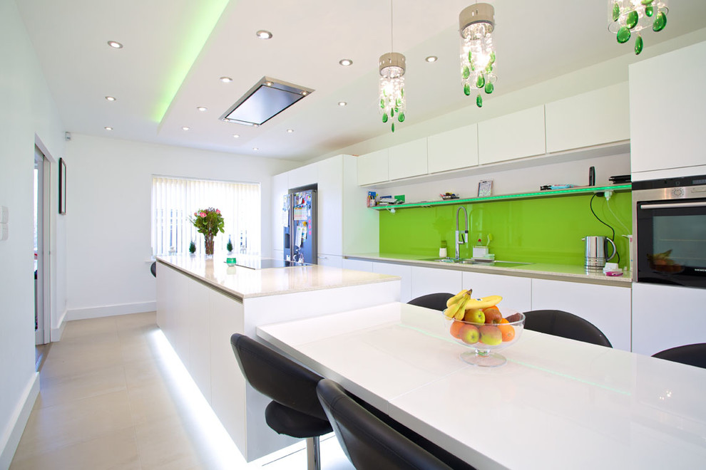 Inspiration for a medium sized contemporary galley kitchen/diner in Hampshire with an integrated sink, flat-panel cabinets, white cabinets, composite countertops, green splashback, glass sheet splashback, stainless steel appliances, porcelain flooring and an island.