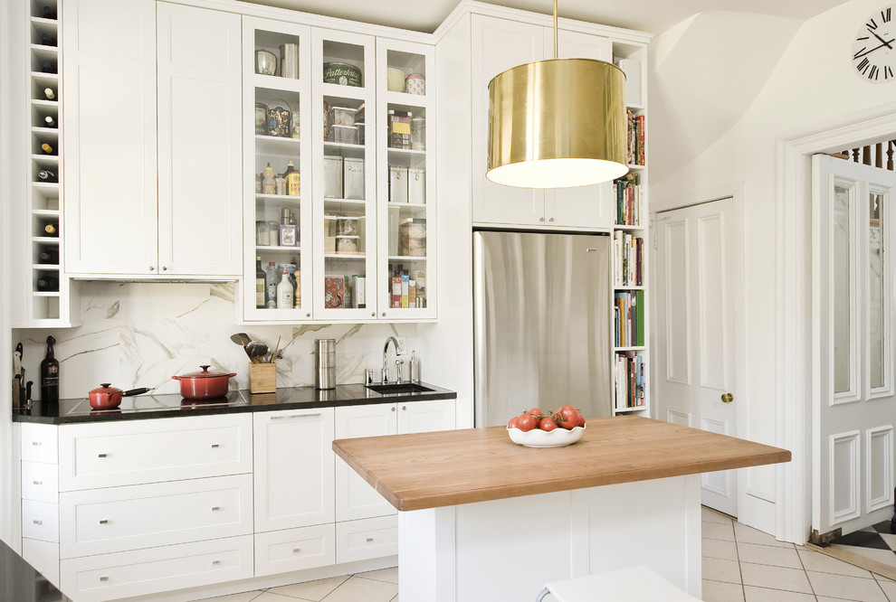 Klassisk inredning av ett kök, med luckor med infälld panel, vita skåp, vitt stänkskydd, stänkskydd i sten och rostfria vitvaror