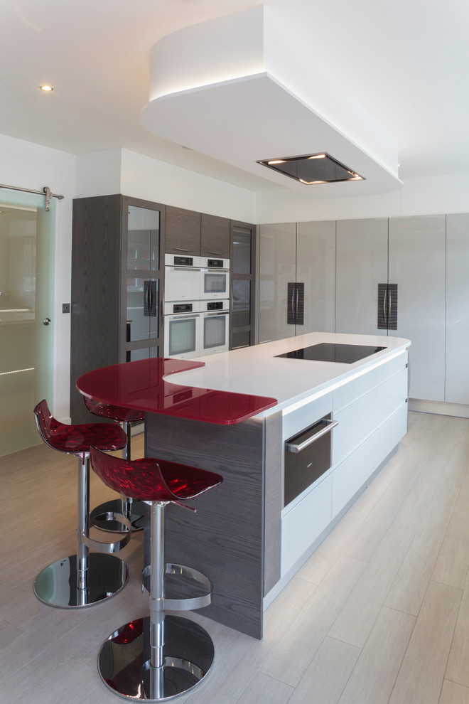 Photo of a large modern l-shaped kitchen/diner in Other with a double-bowl sink, flat-panel cabinets, white cabinets, laminate countertops, grey splashback, glass sheet splashback and an island.