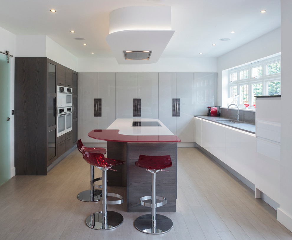 Moderne Küche mit Doppelwaschbecken, flächenbündigen Schrankfronten, Laminat-Arbeitsplatte, Küchenrückwand in Grau, Glasrückwand, Kücheninsel, hellem Holzboden und roter Arbeitsplatte in Sonstige