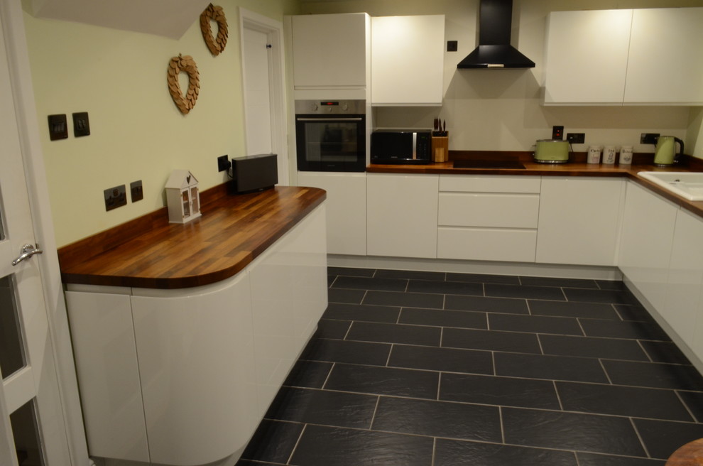 Design ideas for a small modern l-shaped kitchen/diner in Other with a double-bowl sink, beaded cabinets, wood worktops, beige splashback, stainless steel appliances and slate flooring.