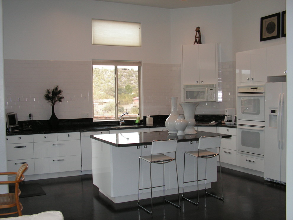 Idéer för att renovera ett mellanstort funkis kök, med en undermonterad diskho, släta luckor, vita skåp, granitbänkskiva, vitt stänkskydd, stänkskydd i tunnelbanekakel, vita vitvaror, betonggolv och en köksö