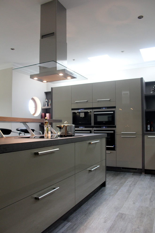 This is an example of a large modern u-shaped open plan kitchen in Glasgow with a double-bowl sink, flat-panel cabinets, stainless steel appliances, an island, black cabinets, glass worktops, black splashback, glass sheet splashback, dark hardwood flooring and black floors.