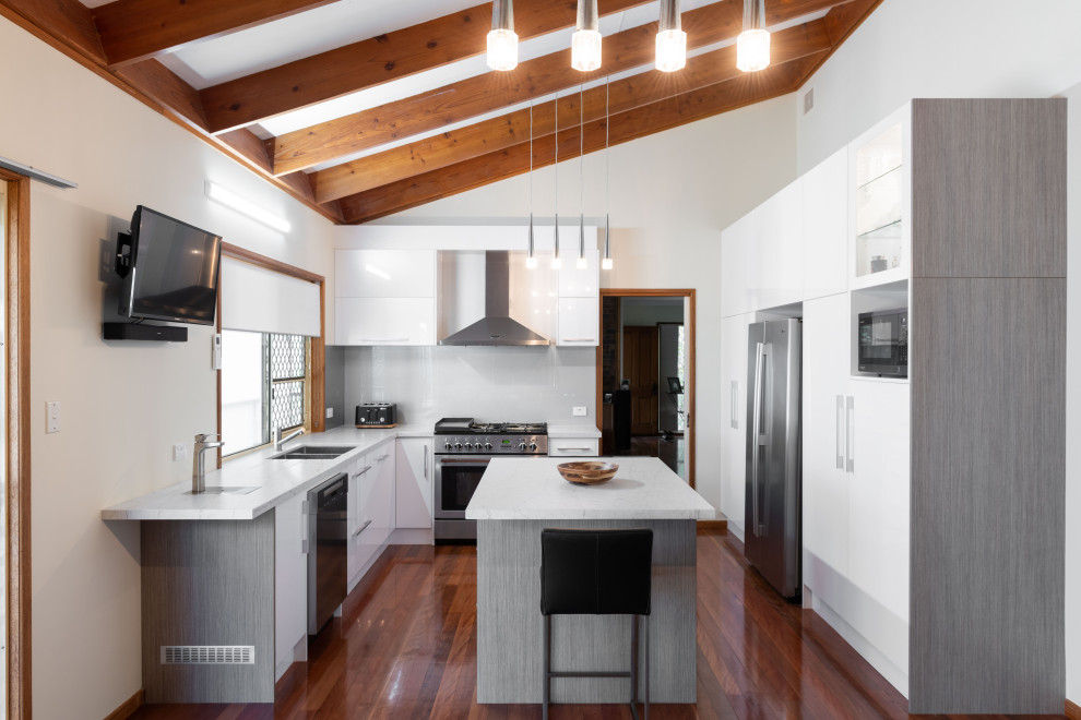 Moderne Küche in U-Form mit Einbauwaschbecken, flächenbündigen Schrankfronten, weißen Schränken, Küchengeräten aus Edelstahl, dunklem Holzboden, Kücheninsel, braunem Boden und weißer Arbeitsplatte in Brisbane
