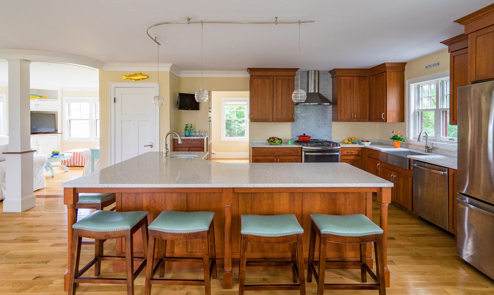 Example of a mid-sized beach style l-shaped light wood floor eat-in kitchen design in Boston with a farmhouse sink, shaker cabinets, medium tone wood cabinets, quartz countertops, blue backsplash, subway tile backsplash, stainless steel appliances and an island
