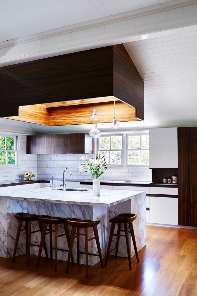 Example of a trendy l-shaped medium tone wood floor kitchen design in Brisbane with an undermount sink, flat-panel cabinets, white cabinets, white backsplash, subway tile backsplash and an island