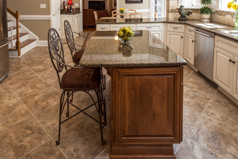 Eat-in kitchen - large traditional u-shaped porcelain tile eat-in kitchen idea in Charlotte with a single-bowl sink, raised-panel cabinets, white cabinets, granite countertops, beige backsplash, stone tile backsplash, stainless steel appliances and an island