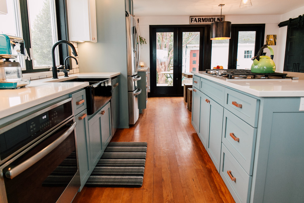 Inspiration for a mid-sized farmhouse medium tone wood floor and brown floor open concept kitchen remodel in Seattle with a farmhouse sink, shaker cabinets, blue cabinets, quartz countertops, white backsplash, ceramic backsplash, stainless steel appliances, an island and white countertops
