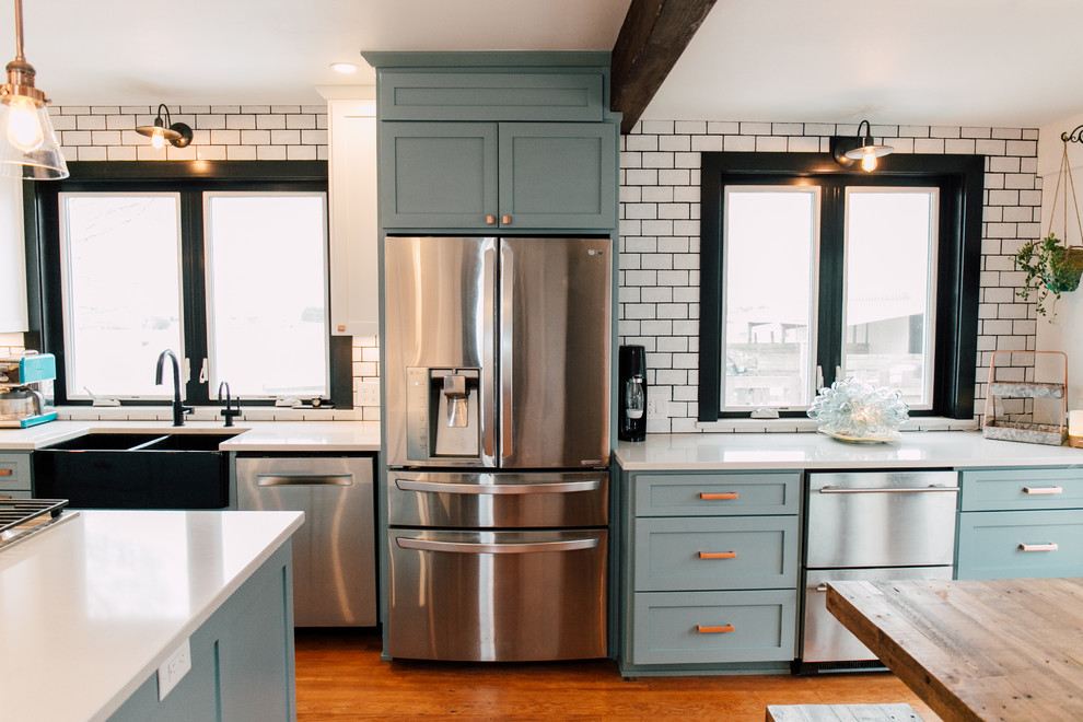 Exempel på ett mellanstort lantligt vit vitt kök med öppen planlösning, med en rustik diskho, skåp i shakerstil, blå skåp, bänkskiva i kvarts, vitt stänkskydd, stänkskydd i keramik, rostfria vitvaror, mellanmörkt trägolv, en köksö och brunt golv