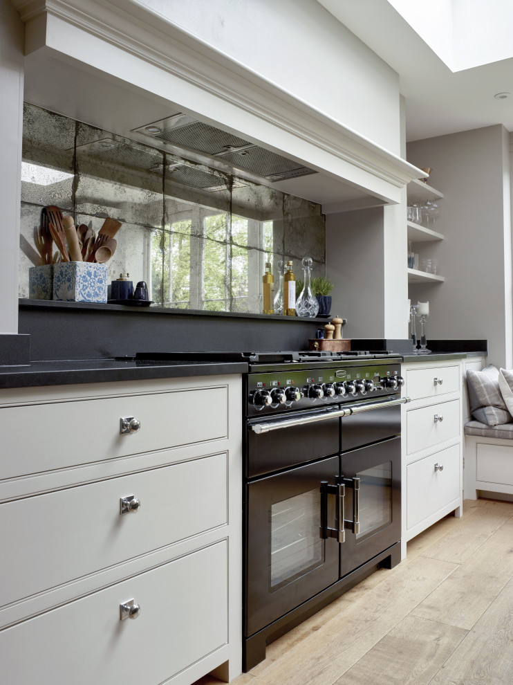 Idéer för att renovera ett mellanstort vintage svart svart kök, med en enkel diskho, skåp i shakerstil, vita skåp, granitbänkskiva, spegel som stänkskydd, svarta vitvaror, ljust trägolv, en köksö och beiget golv