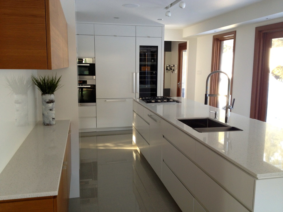 Modern inredning av ett mellanstort kök, med en dubbel diskho, släta luckor, vita skåp, bänkskiva i kvarts, vitt stänkskydd, glaspanel som stänkskydd, integrerade vitvaror, klinkergolv i keramik och en köksö