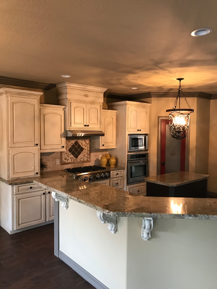 Photo of a medium sized traditional u-shaped kitchen/diner in Houston with a built-in sink, raised-panel cabinets, white cabinets, tile countertops, beige splashback, ceramic splashback, stainless steel appliances, ceramic flooring, an island and beige floors.
