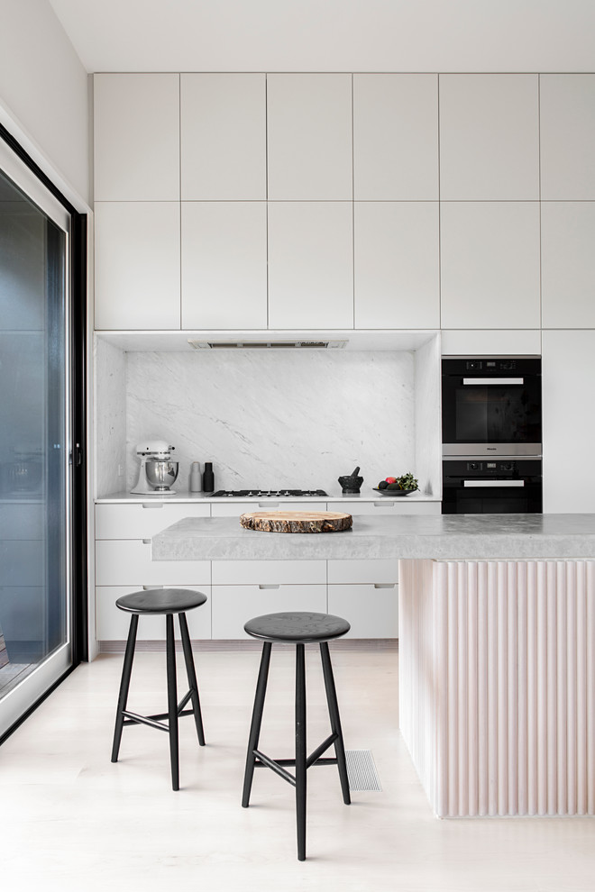 Источник вдохновения для домашнего уюта: кухня в скандинавском стиле с белыми фасадами, столешницей из бетона, белым фартуком, фартуком из каменной плиты, черной техникой, светлым паркетным полом и островом
