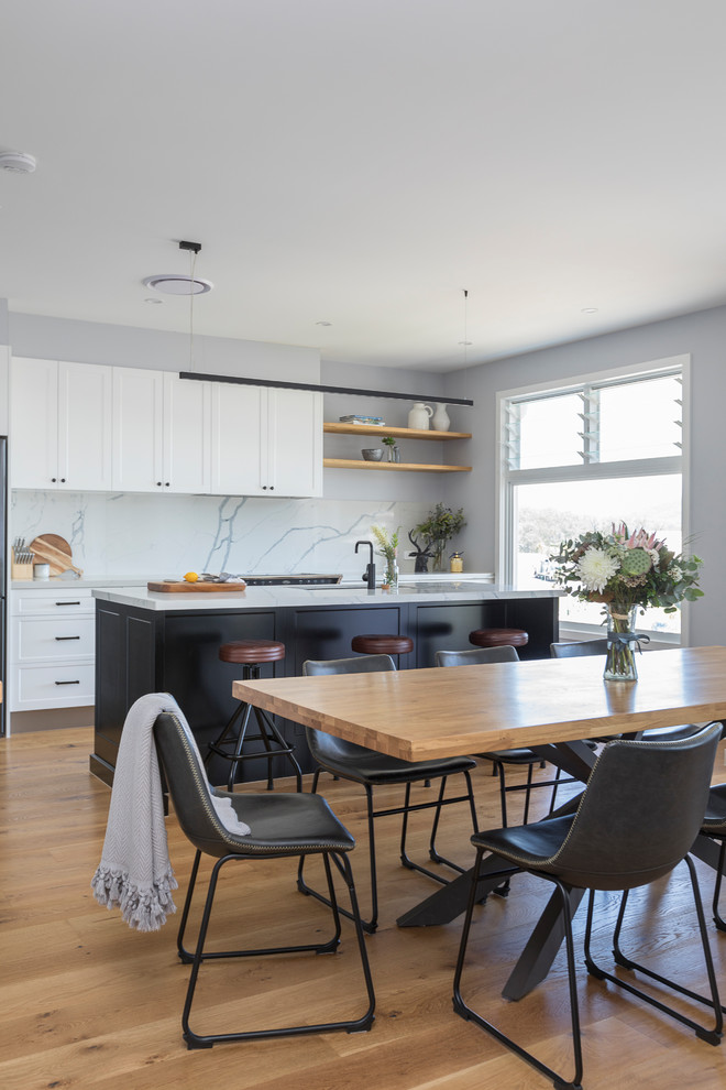 Design ideas for a medium sized coastal galley open plan kitchen in Gold Coast - Tweed with an integrated sink, raised-panel cabinets, white cabinets, marble worktops, white splashback, marble splashback, black appliances, medium hardwood flooring, an island and brown floors.