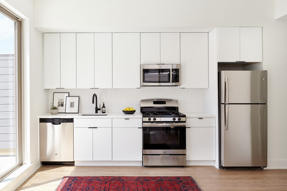 Foto på ett litet funkis kök, med en undermonterad diskho, släta luckor, vita skåp, bänkskiva i kvarts, vitt stänkskydd, stänkskydd i keramik, rostfria vitvaror, ljust trägolv och beiget golv