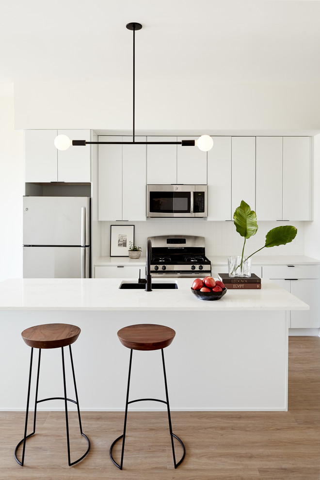 Exempel på ett litet modernt kök, med en undermonterad diskho, släta luckor, vita skåp, bänkskiva i kvarts, vitt stänkskydd, rostfria vitvaror, ljust trägolv, en köksö och beiget golv