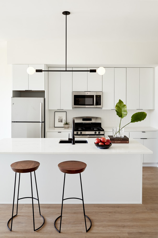 Kitchen - small contemporary light wood floor and beige floor kitchen idea in Philadelphia with an undermount sink, flat-panel cabinets, white cabinets, quartz countertops, white backsplash, stainless steel appliances and an island