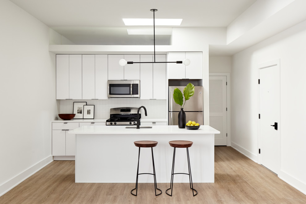 Small trendy galley light wood floor and beige floor open concept kitchen photo in Philadelphia with an undermount sink, flat-panel cabinets, white cabinets, quartz countertops, white backsplash, ceramic backsplash, stainless steel appliances and an island