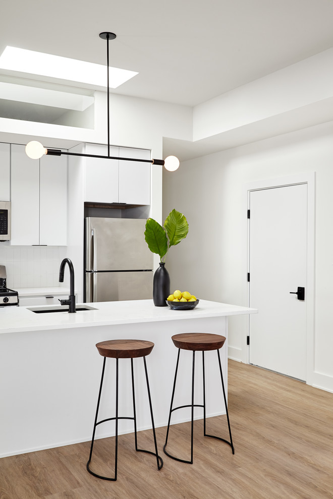 Example of a small trendy galley light wood floor and beige floor open concept kitchen design in Philadelphia with an undermount sink, flat-panel cabinets, white cabinets, quartz countertops, white backsplash, ceramic backsplash, stainless steel appliances and an island