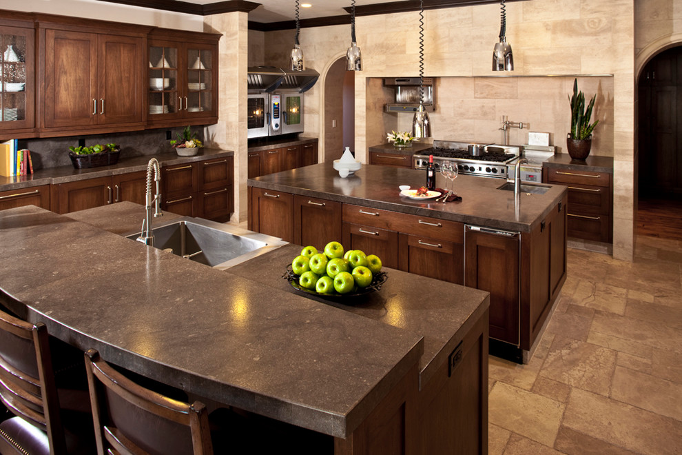 Example of a large mountain style u-shaped ceramic tile eat-in kitchen design in Las Vegas with a single-bowl sink, raised-panel cabinets, dark wood cabinets, solid surface countertops, beige backsplash, ceramic backsplash, stainless steel appliances and two islands