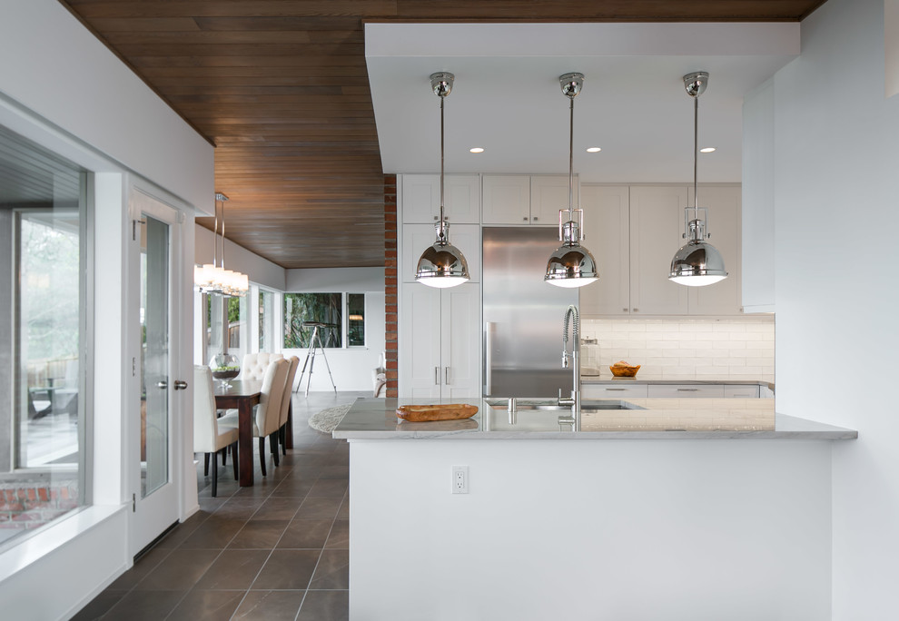 Example of a mid-sized trendy u-shaped porcelain tile enclosed kitchen design in Seattle with an undermount sink, shaker cabinets, white cabinets, marble countertops, white backsplash, ceramic backsplash, stainless steel appliances and a peninsula