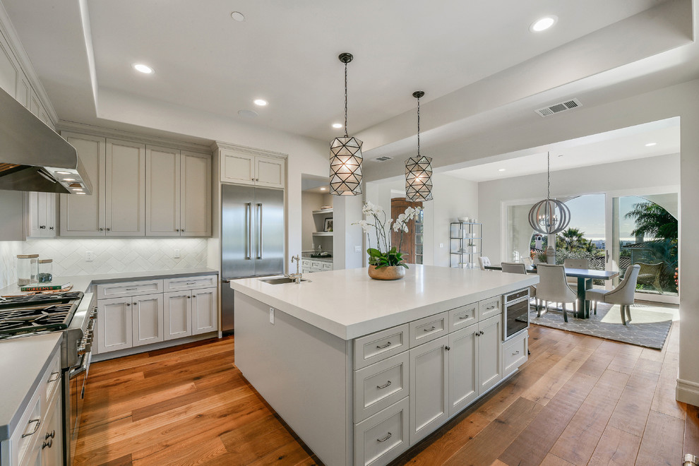 Eat-in kitchen - large mediterranean u-shaped medium tone wood floor eat-in kitchen idea in San Francisco with a farmhouse sink, shaker cabinets, gray cabinets, quartzite countertops, white backsplash, ceramic backsplash, stainless steel appliances and an island