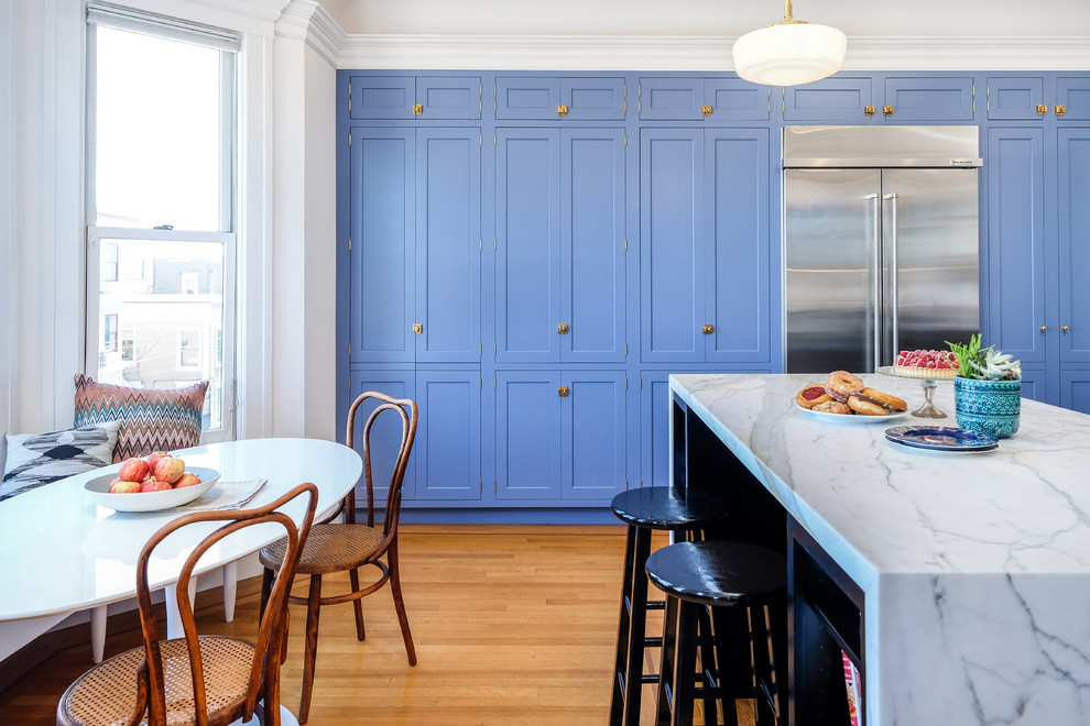 Diseño de cocina comedor clásica renovada con armarios estilo shaker, puertas de armario azules, electrodomésticos de acero inoxidable, suelo de madera en tonos medios, una isla, suelo marrón y encimeras grises