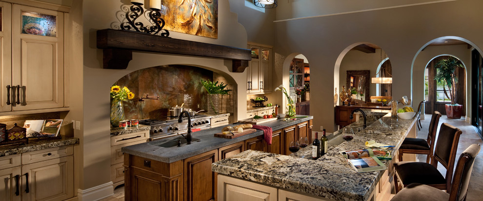 Exempel på ett mycket stort medelhavsstil kök, med en undermonterad diskho, luckor med upphöjd panel, granitbänkskiva, grönt stänkskydd, stänkskydd i stenkakel, rostfria vitvaror, travertin golv, flera köksöar och beige skåp