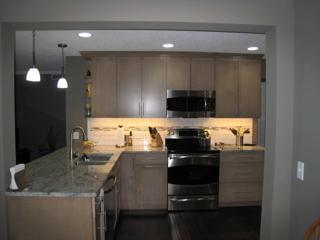 Photo of a small traditional grey and cream l-shaped kitchen/diner in Minneapolis with a double-bowl sink, recessed-panel cabinets, grey cabinets, granite worktops, white splashback, ceramic splashback, stainless steel appliances and dark hardwood flooring.