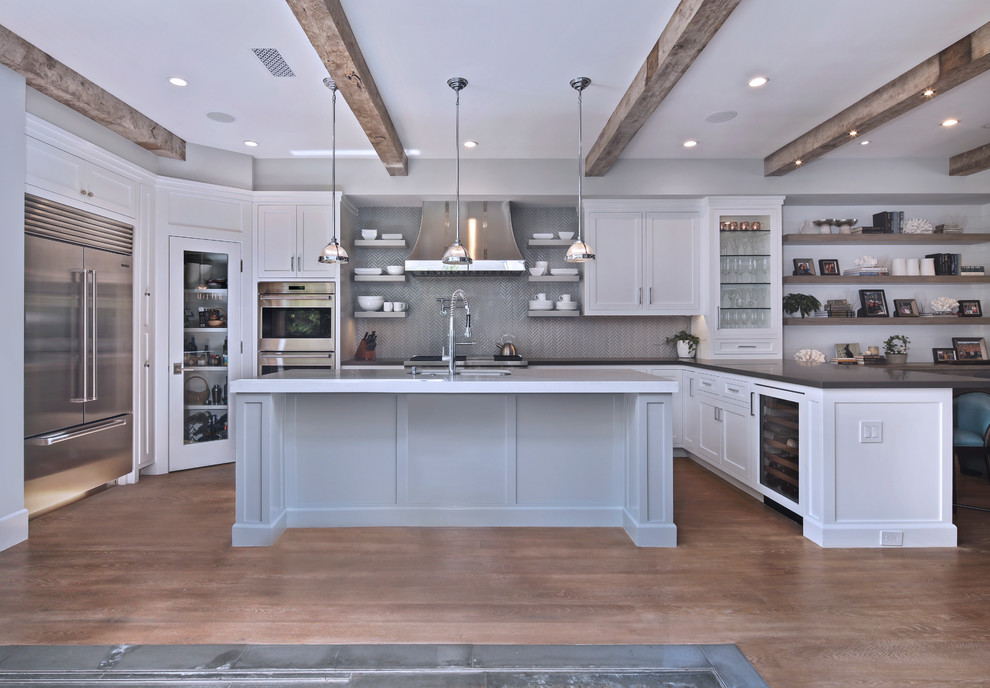 Offene Maritime Küche in grau-weiß mit Unterbauwaschbecken, Glasfronten, weißen Schränken, Küchenrückwand in Grau, Küchengeräten aus Edelstahl, braunem Holzboden und Kücheninsel in Orange County
