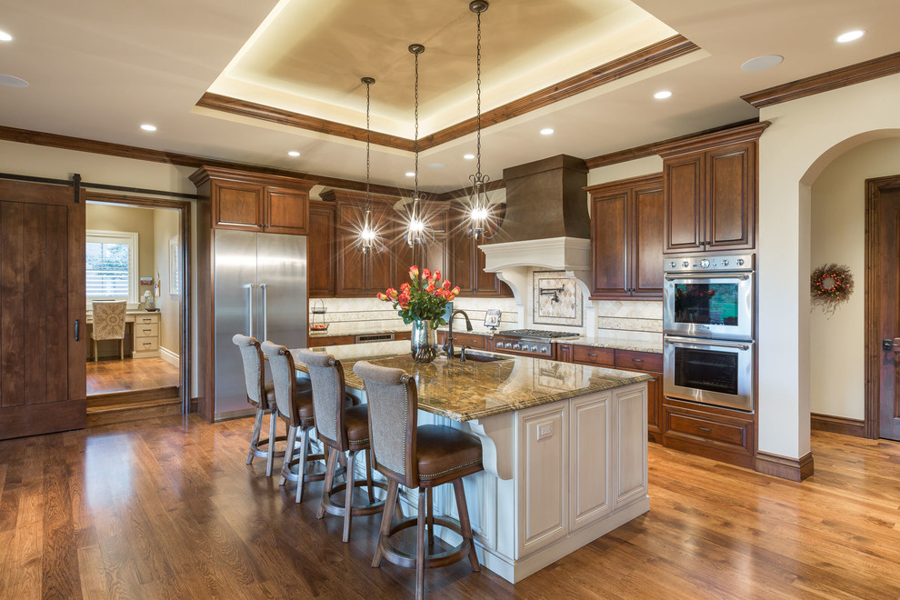 Large mountain style l-shaped medium tone wood floor and brown floor eat-in kitchen photo in Denver with raised-panel cabinets, dark wood cabinets, granite countertops, stainless steel appliances, an island, an undermount sink, multicolored backsplash, ceramic backsplash and multicolored countertops
