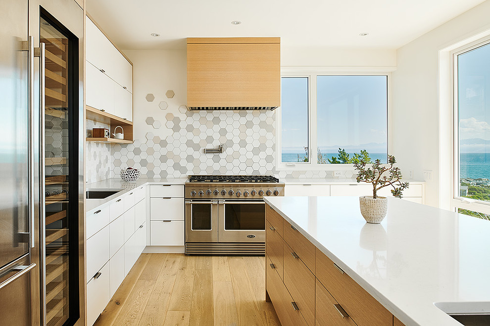 Photo of a medium sized modern l-shaped open plan kitchen in Other with a single-bowl sink, flat-panel cabinets, light wood cabinets, engineered stone countertops, multi-coloured splashback, ceramic splashback, stainless steel appliances, light hardwood flooring, an island and white worktops.