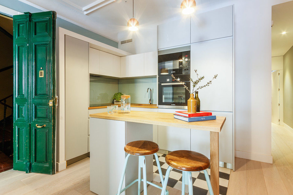 Inspiration for a medium sized contemporary l-shaped kitchen in Madrid with flat-panel cabinets, wood worktops, an island, green splashback, glass sheet splashback, black appliances and light hardwood flooring.