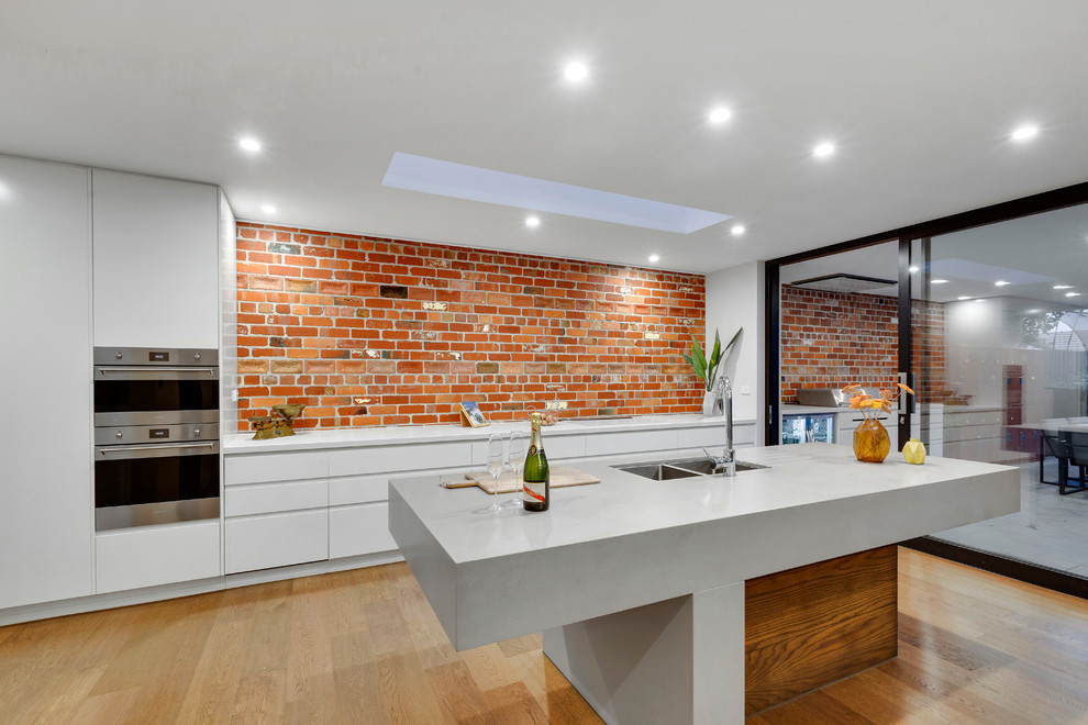 Inspiration for a large modern open plan kitchen in Melbourne with a submerged sink, white cabinets, composite countertops, brick splashback, stainless steel appliances, an island and grey worktops.