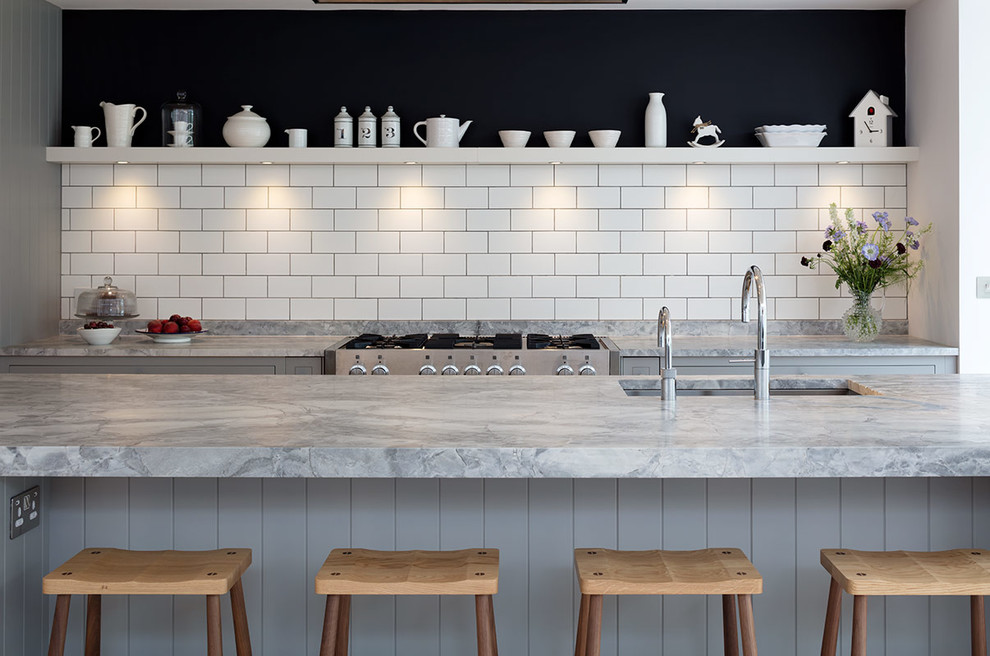 Large contemporary single-wall open plan kitchen in London with a submerged sink, marble worktops, white splashback, cement tile splashback, light hardwood flooring, an island, beige floors and grey worktops.
