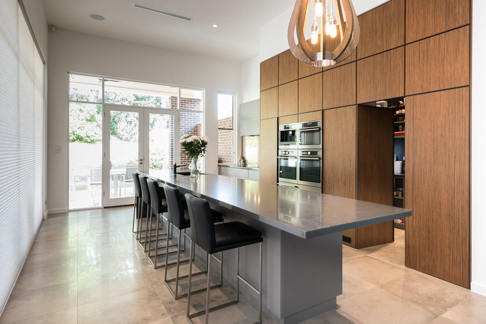 This is an example of a contemporary kitchen in Adelaide with a single-bowl sink, flat-panel cabinets, brown cabinets, stainless steel appliances, an island and beige floors.