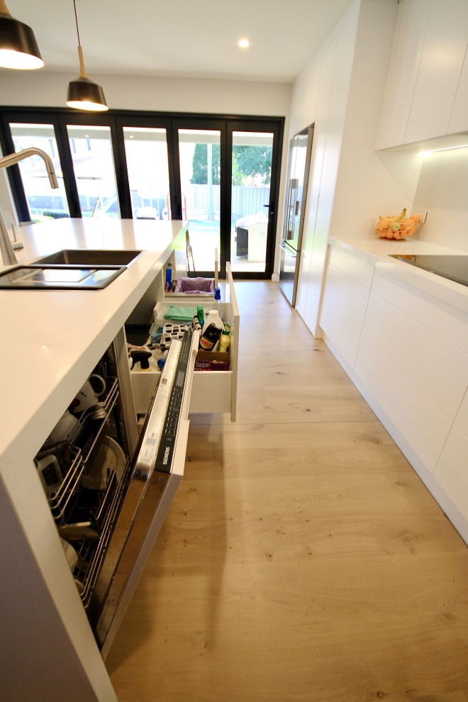 Exempel på ett stort modernt vit linjärt vitt kök med öppen planlösning, med en nedsänkt diskho, släta luckor, vita skåp, bänkskiva i kvarts, vitt stänkskydd, stänkskydd i marmor, svarta vitvaror, mellanmörkt trägolv, en köksö och brunt golv