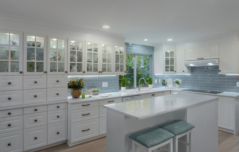 Bild på ett mellanstort, avskilt vintage vit vitt l-kök, med luckor med upphöjd panel, vita skåp, bänkskiva i kvarts, blått stänkskydd, stänkskydd i glaskakel, en köksö, ljust trägolv, brunt golv, en undermonterad diskho och vita vitvaror
