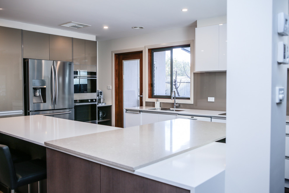 Inspiration for a large contemporary l-shaped kitchen/diner with a submerged sink, flat-panel cabinets, white cabinets, engineered stone countertops, metallic splashback, glass sheet splashback, stainless steel appliances, dark hardwood flooring and multiple islands.